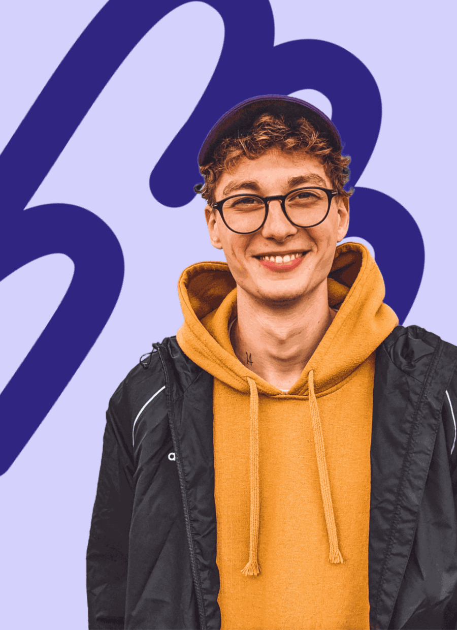 Junger Mann mit Brille, Cap und gelbem Hoodie lächelt in die Kamera